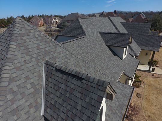 Aerial view of several houses with gray shingled roofs in a suburban neighborhood.