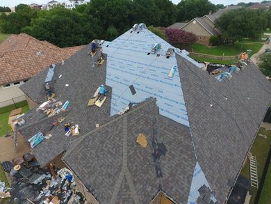 Aerial view of a roof under repair, with workers and exposed blue underlayment on several roof sections