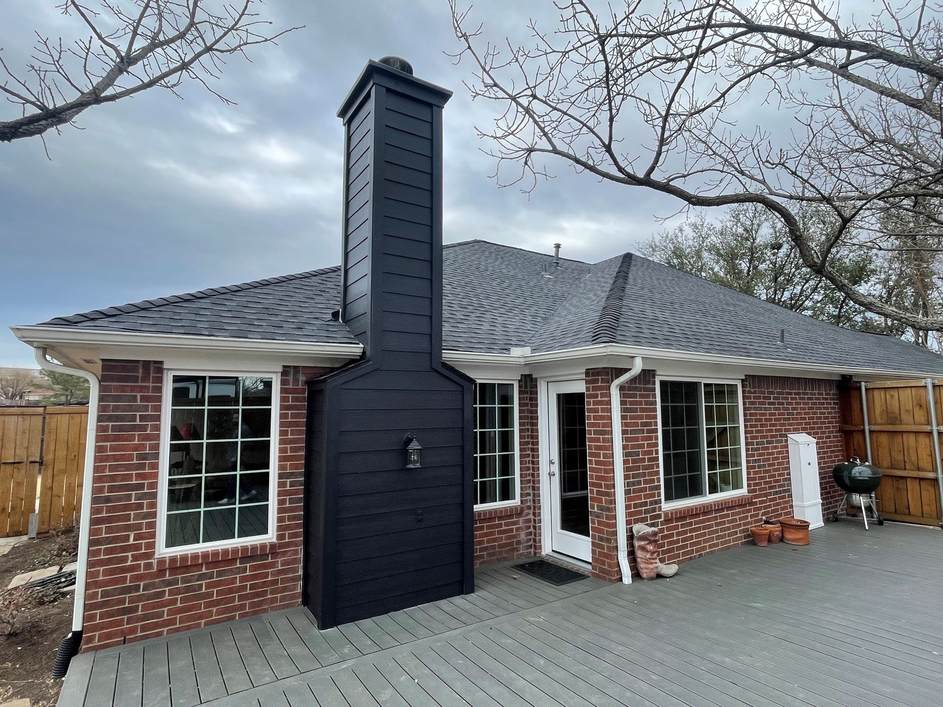 Red brick house with a large black chimney, gray deck, and cloudy sky. Red brick house with a large black chimney, gray deck, and cloudy sky.