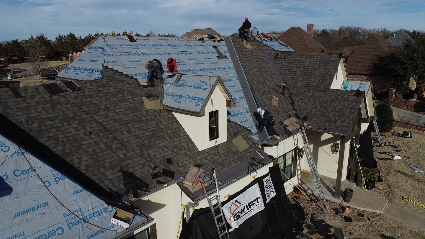 Damaged house roof with workers installing blue underlayment after storm damage