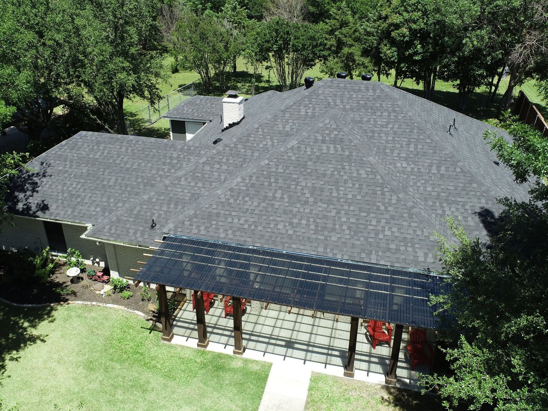 Aerial view of a house with a dark gray roof surrounded by green trees and lawn.