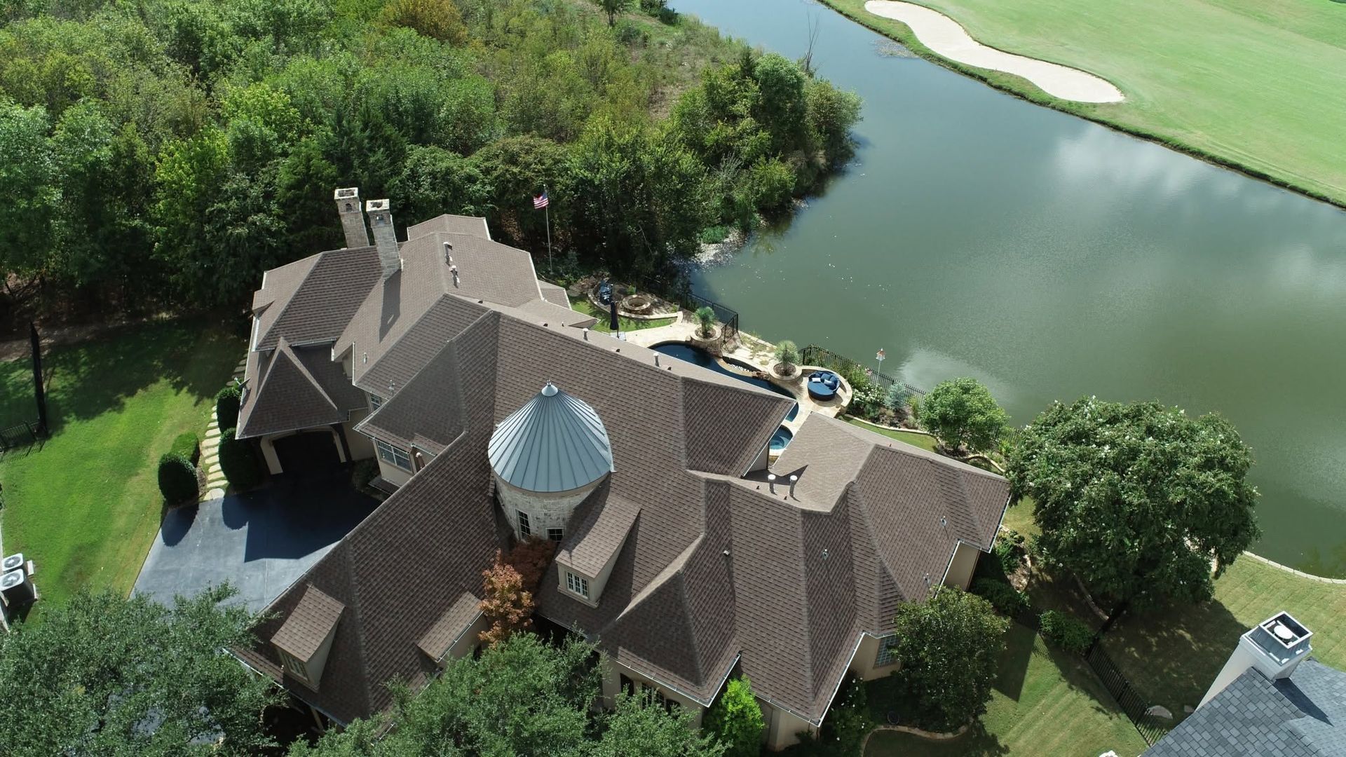 Aerial view of a large brown house with a dome roof beside a winding river and green trees.