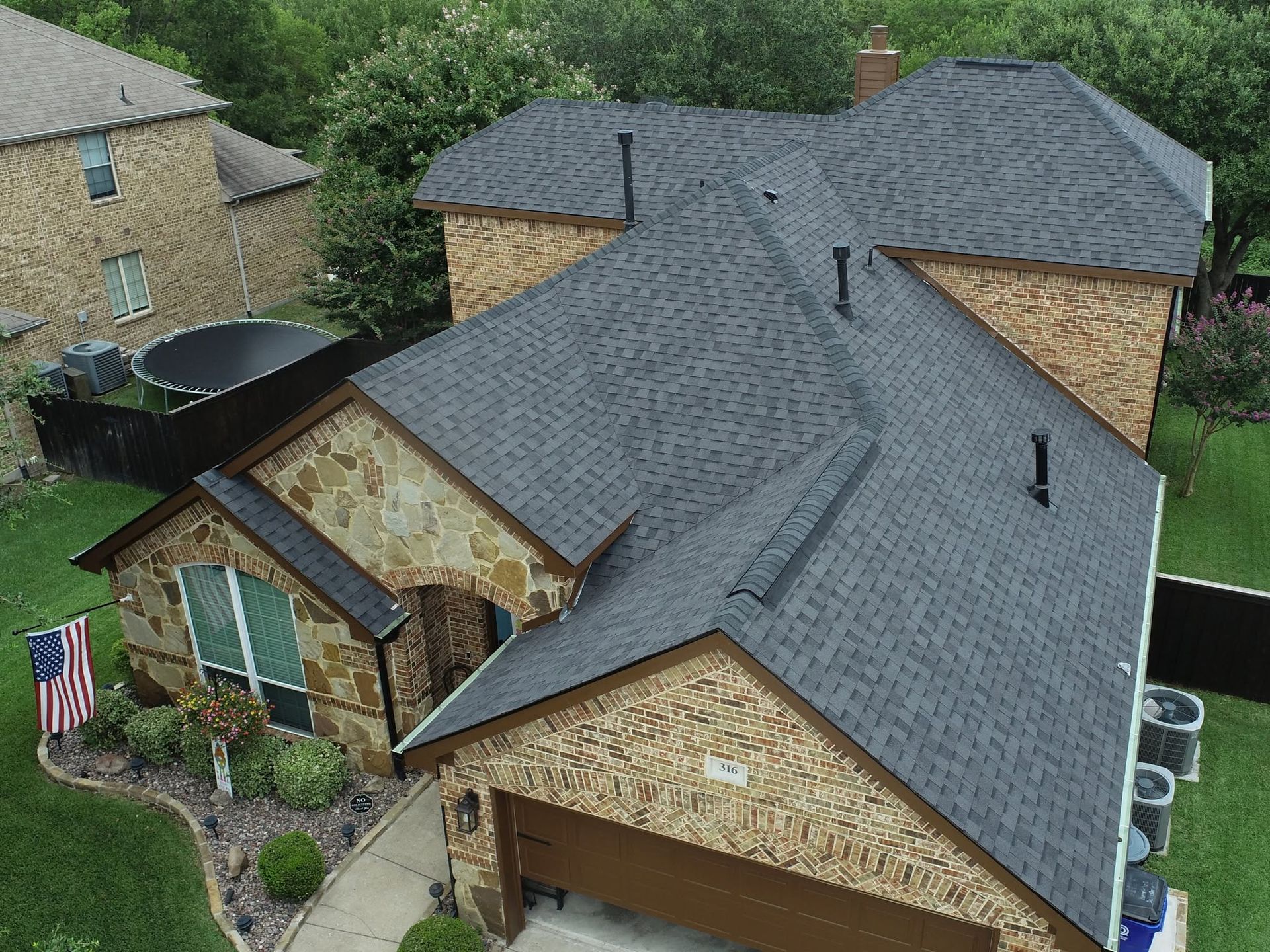 Aerial view of a suburban brick house with a dark gray roof and American flag by the front yard