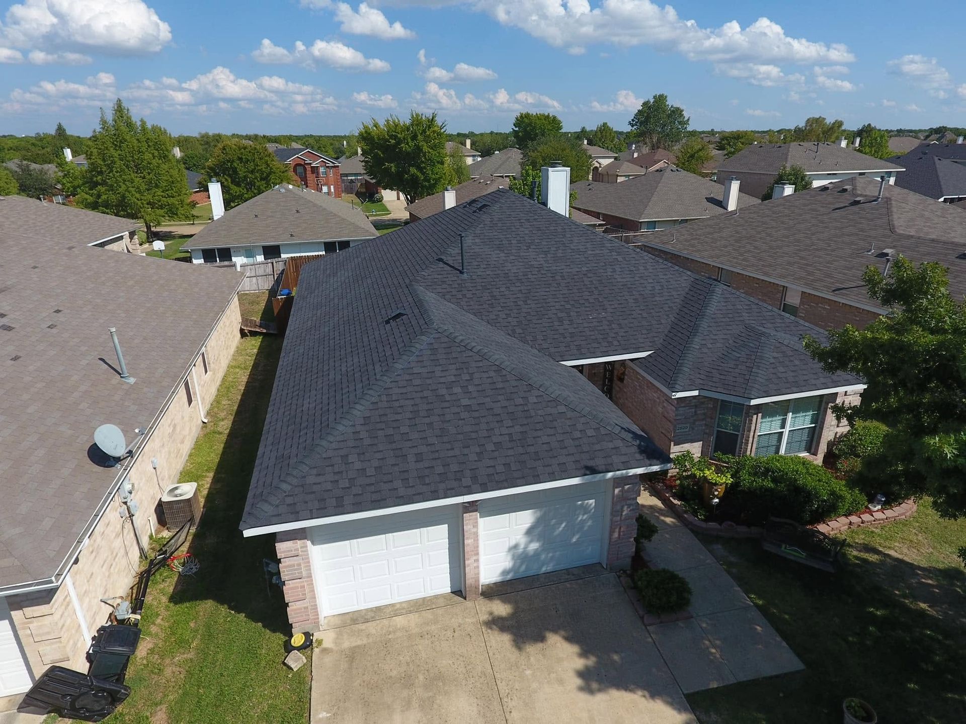 Aerial view of a suburban house with a dark roof and white garage under a blue sky