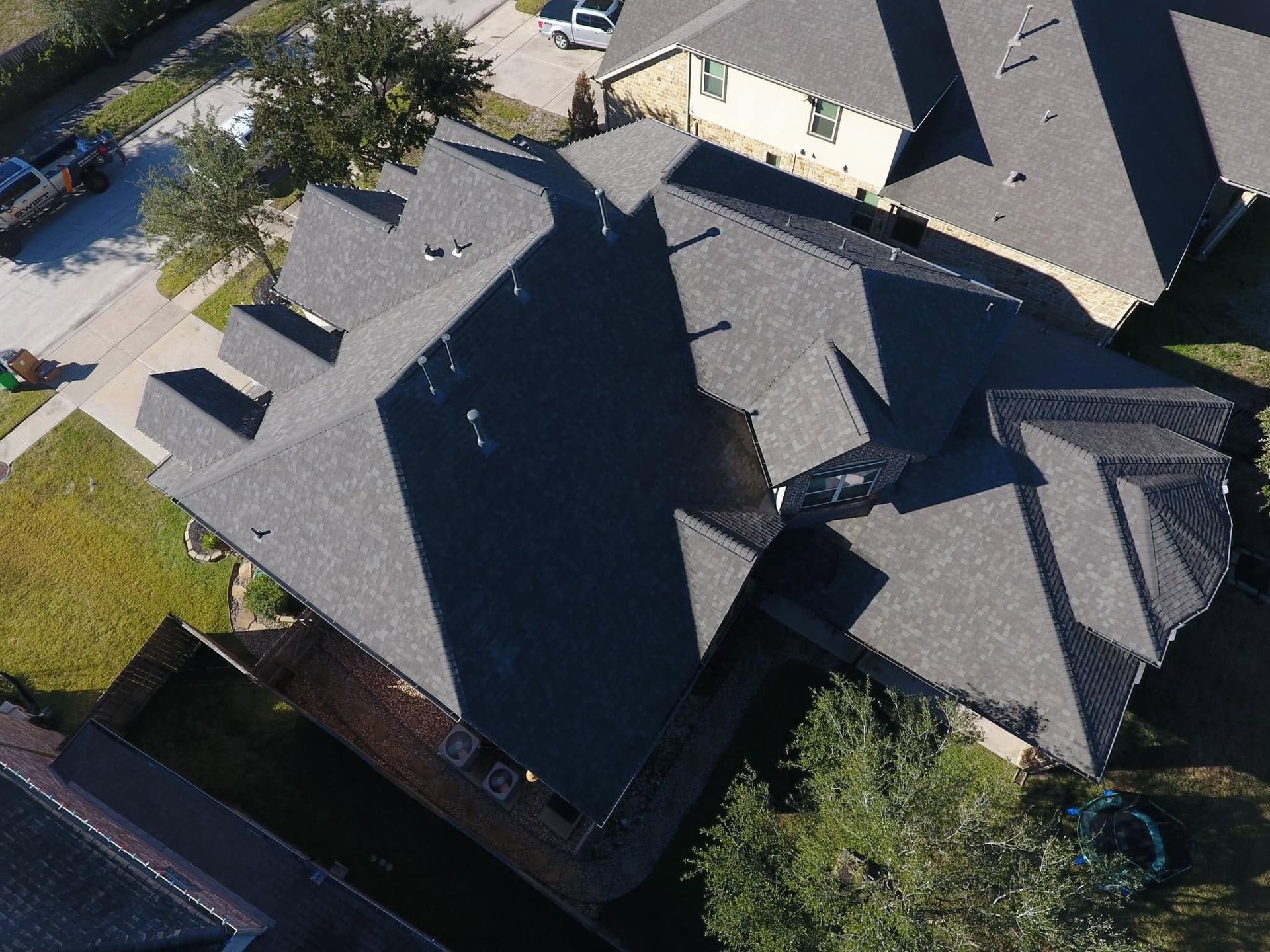 Aerial view of a house with a dark gray roof and surrounding yard trees.