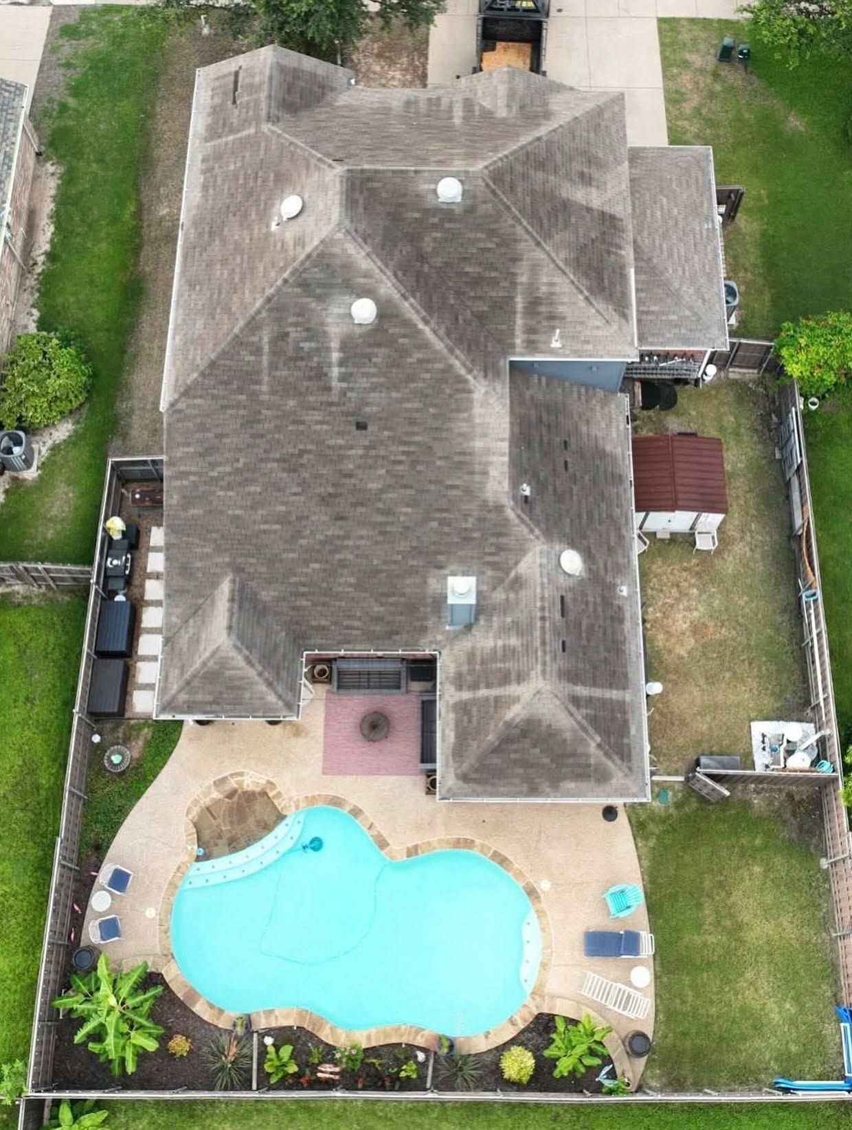 Aerial view of a house with a backyard pool, patio seating, and fenced lawn.