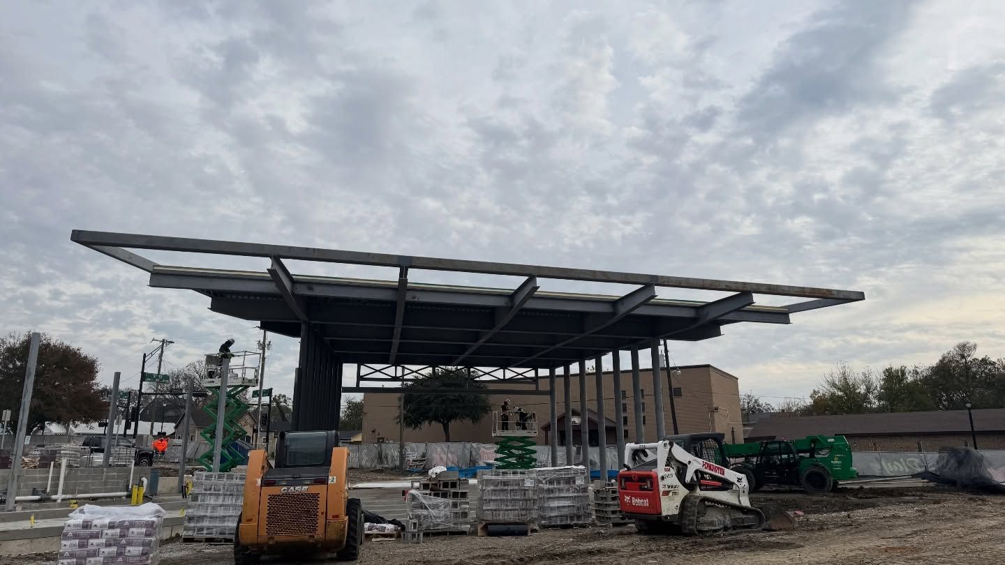 Construction site with large canopy structure, excavator, and building materials under a cloudy sky