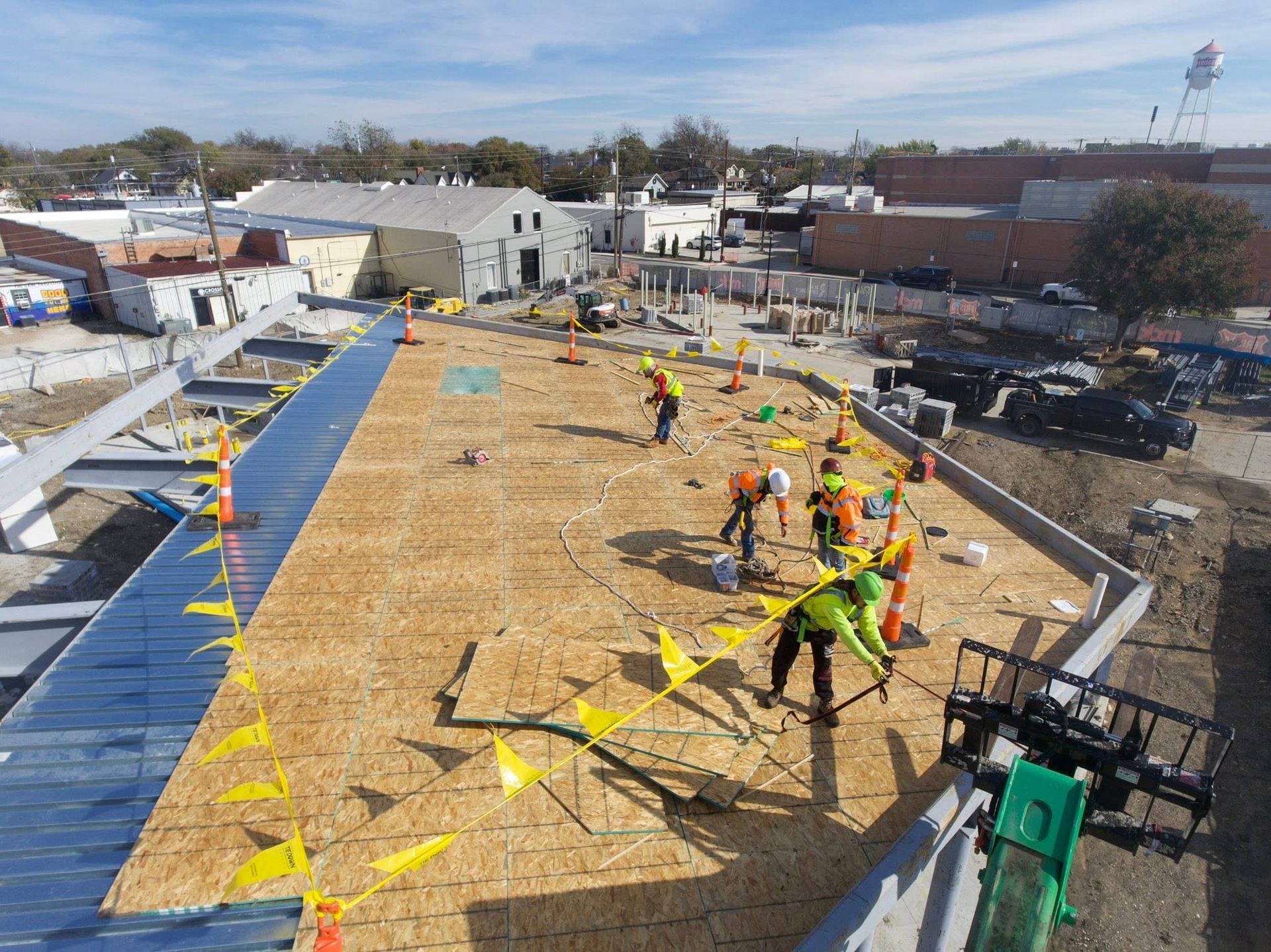 Roofing crew installing plywood sheathing on a large flat roof under construction