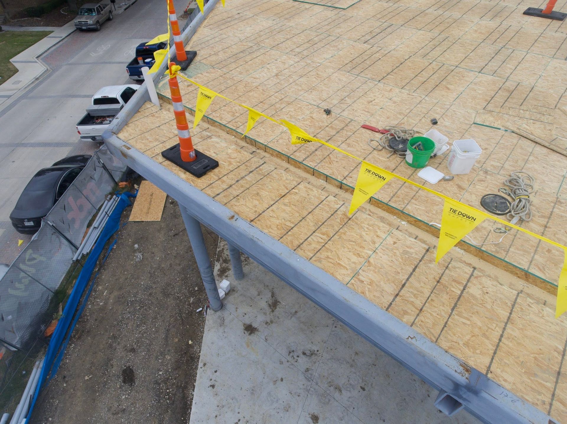 Roof work area with yellow caution tape, traffic cone, tools, and a ladder by the edge of a building
