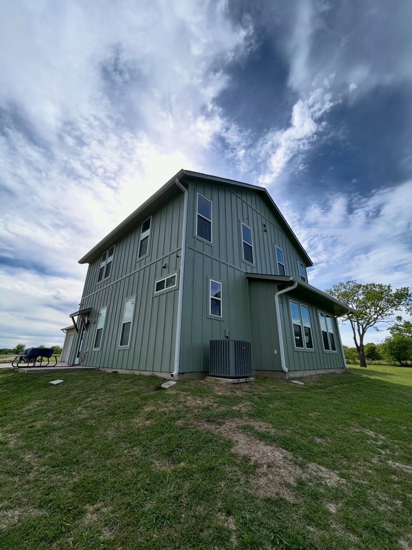 Green two-story house with vertical siding on a grassy hill under a cloudy sky