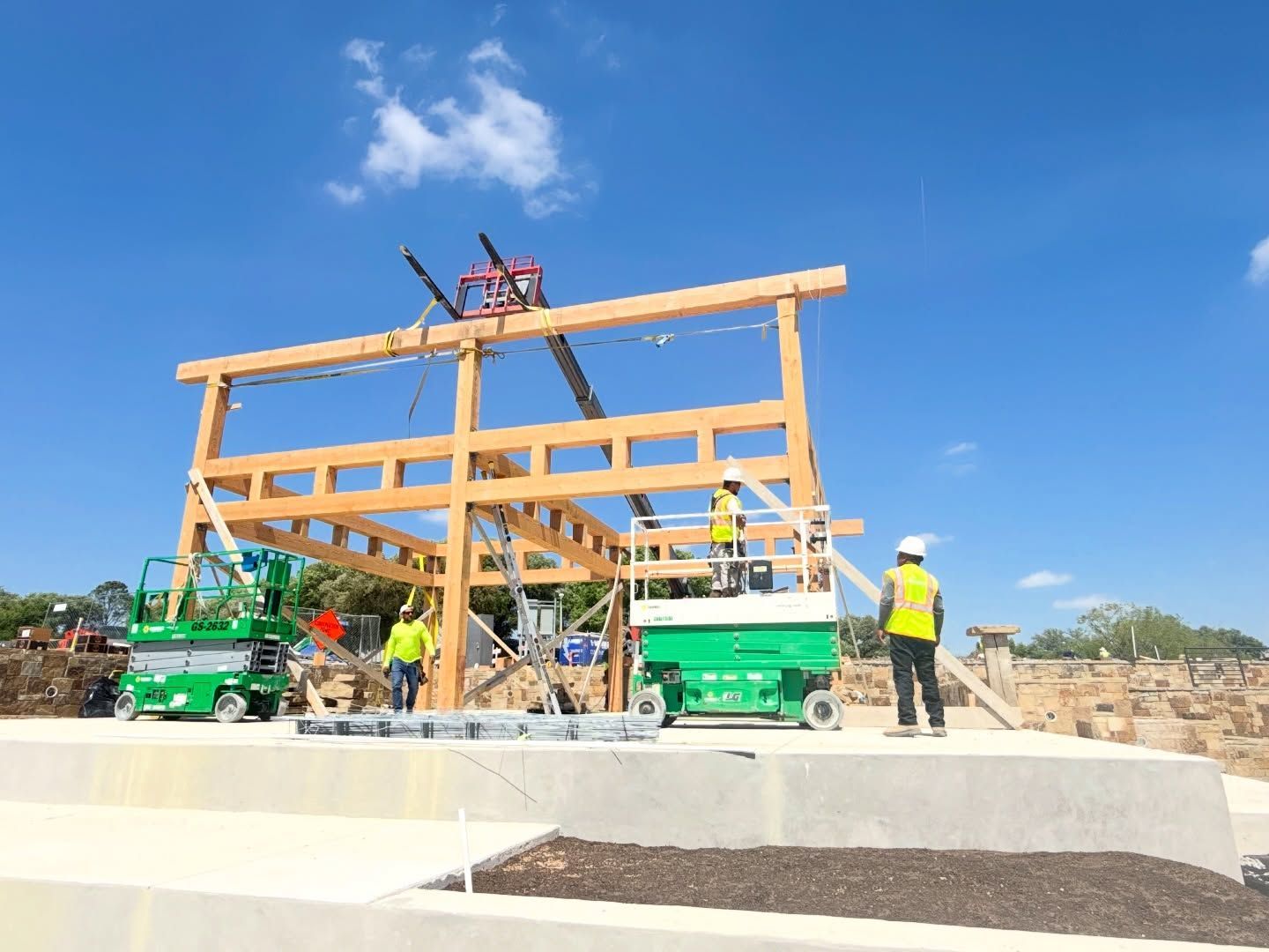 Construction workers assembling a wooden building frame on a concrete site under a clear blue sky