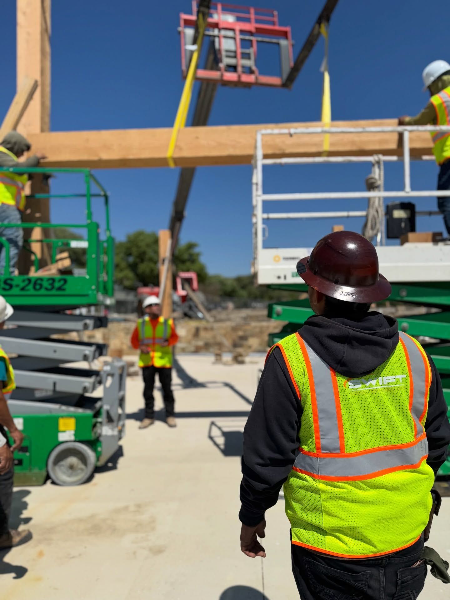 Construction workers guiding a crane-lifted beam overhead on a job site