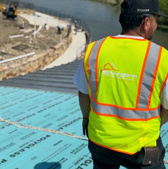Worker in a neon safety vest on a rooftop construction site near water