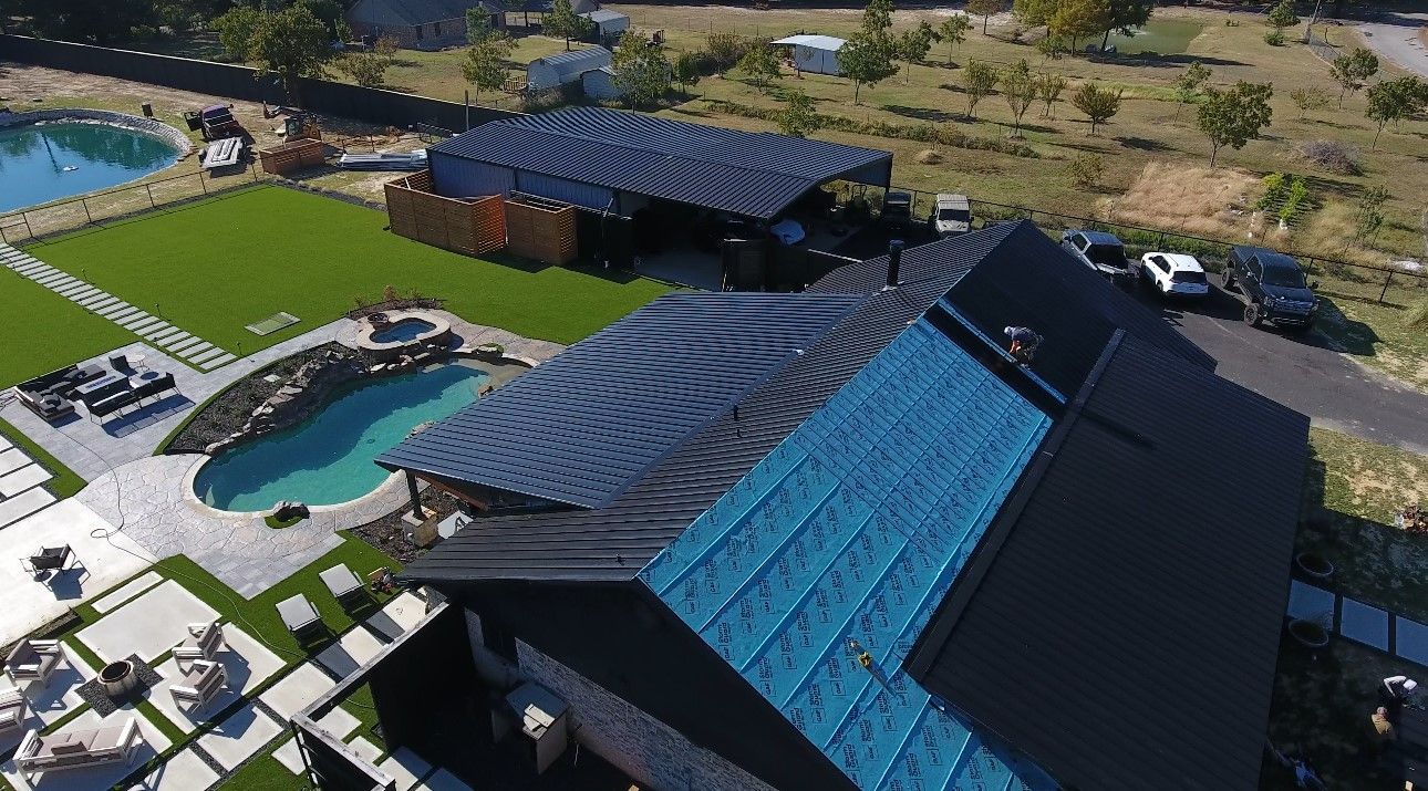 Aerial view of a modern building with a blue roof, curved solar panels, and a swimming pool