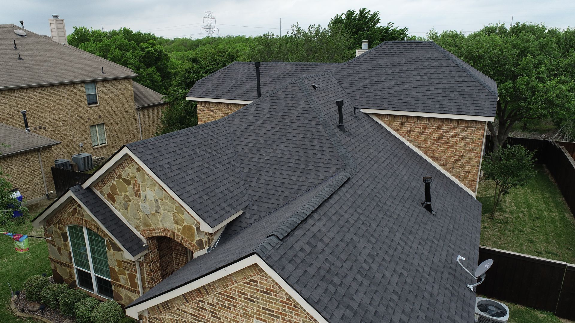 A multi-gabled house with dark gray asphalt shingle roof. The house has tan stone and brick siding.