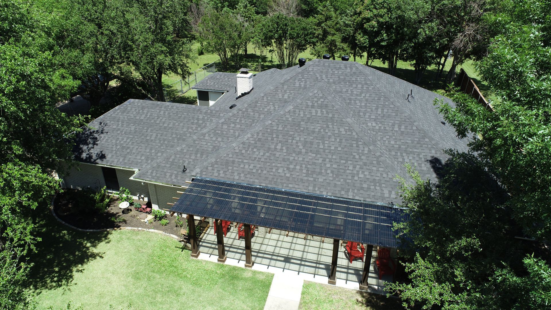 Aerial view of a house with a dark roof surrounded by trees and a green yard
