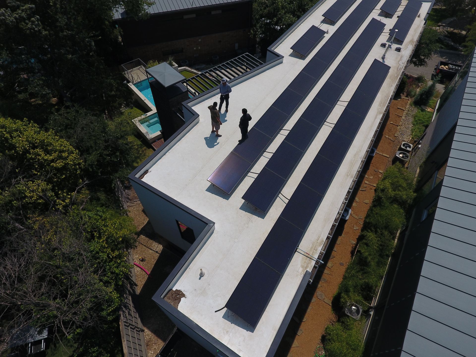 Aerial view of a building rooftop with solar panels. Three people are standing on the roof near the panels.