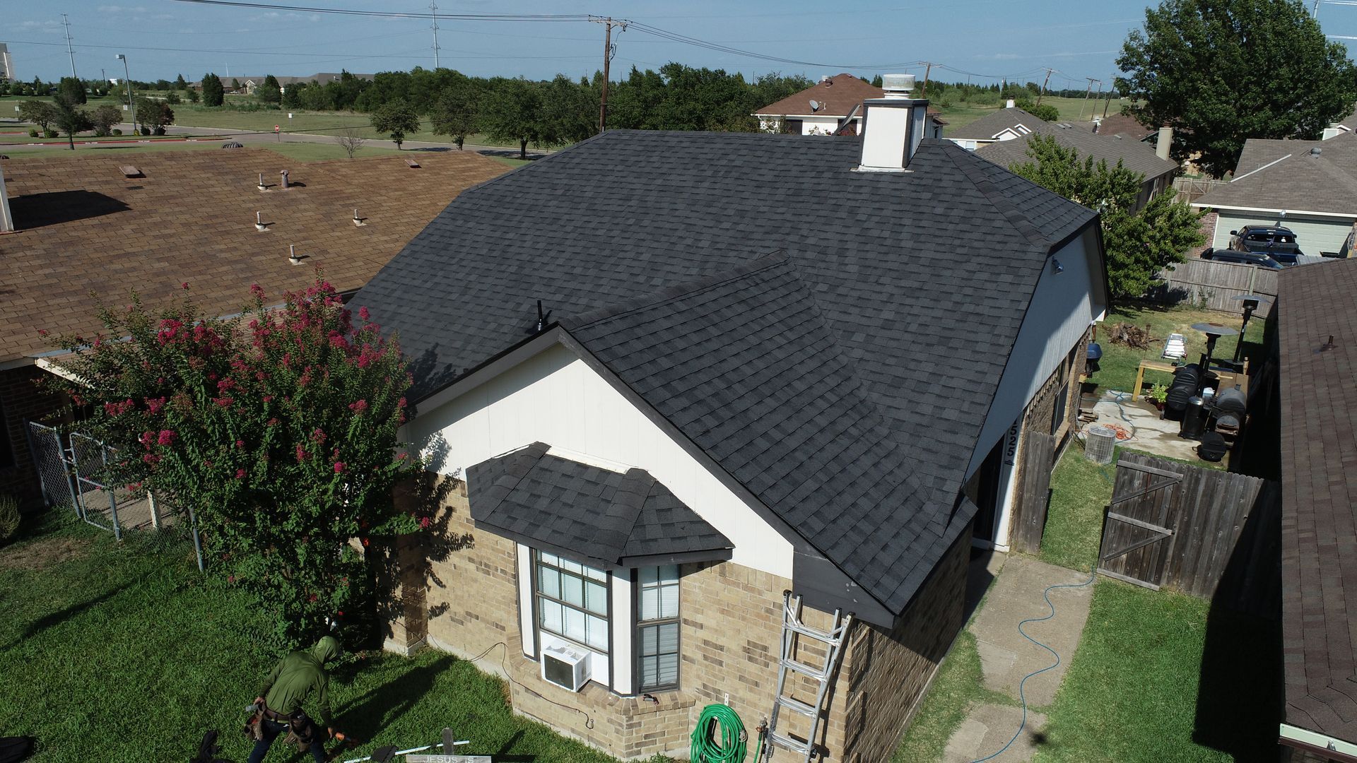 House with a black shingle roof, white walls, and brick accents, viewed from above.