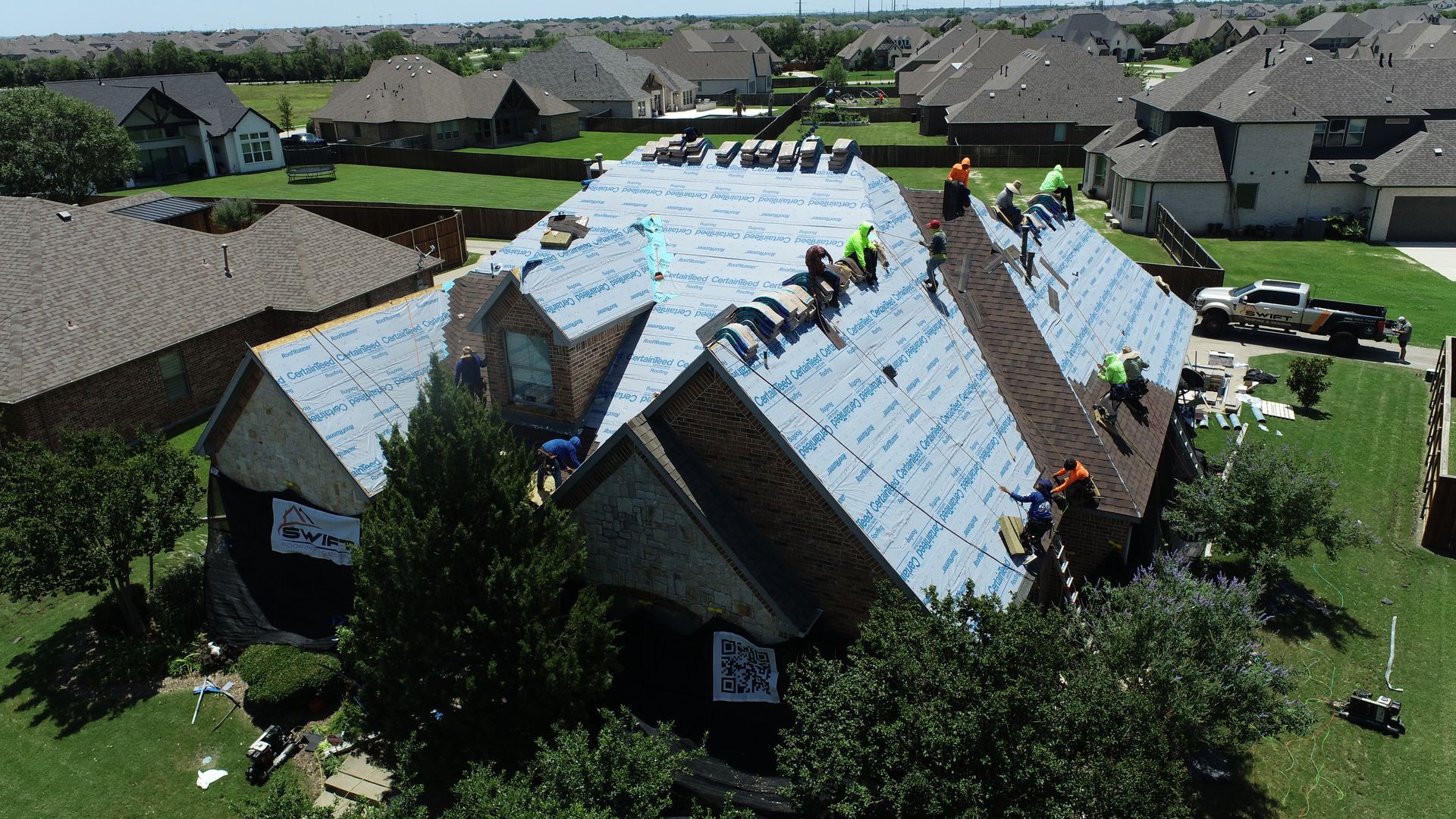 Workers installing a new roof on a suburban house. They are wearing safety vests and hard hats.