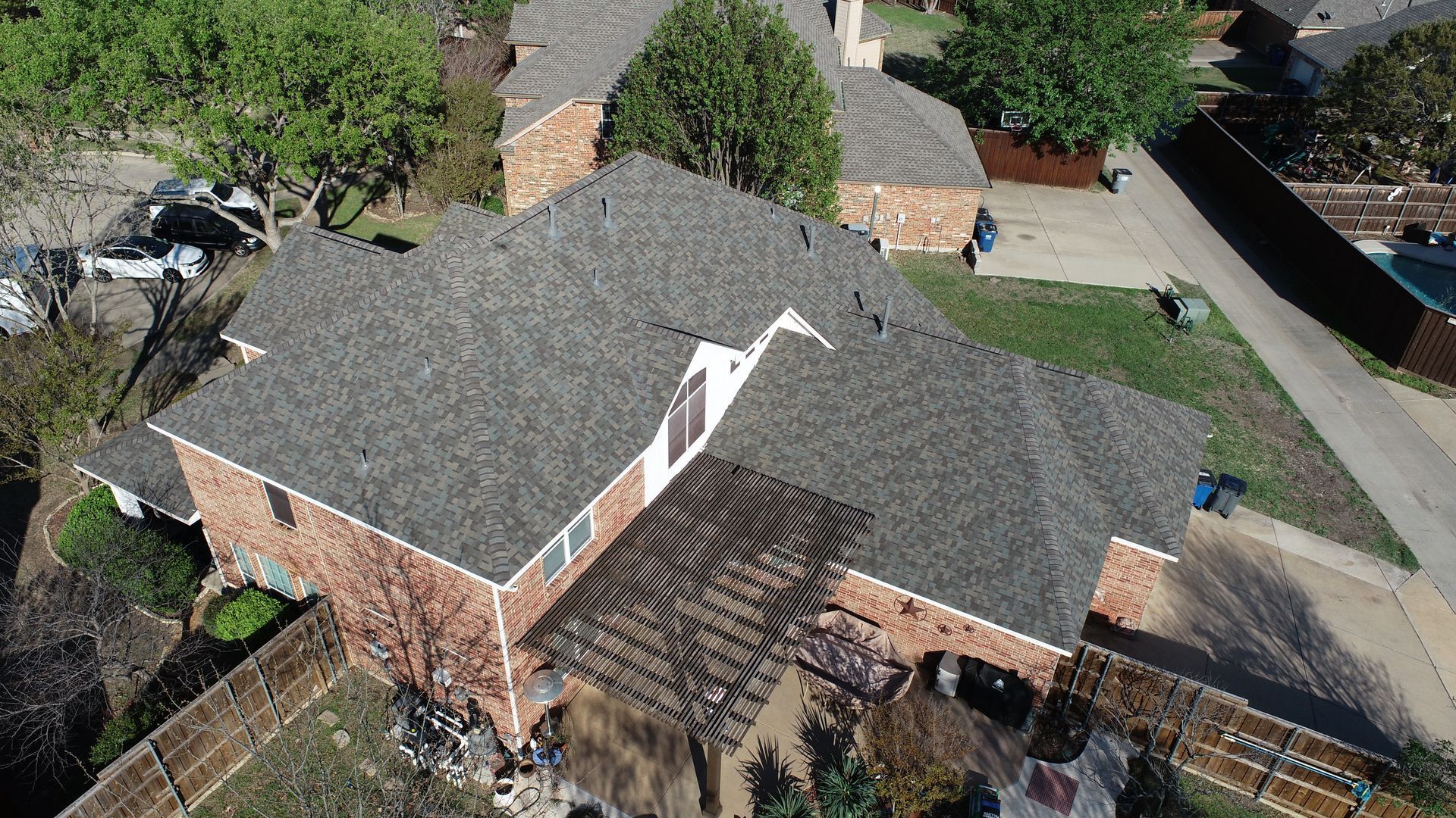 Aerial view of a brick house with a gray roof and a wooden fence in a suburban neighborhood.