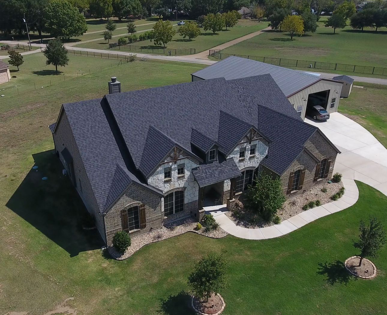 Aerial view of a house with a dark roof and attached garage on a green lawn.