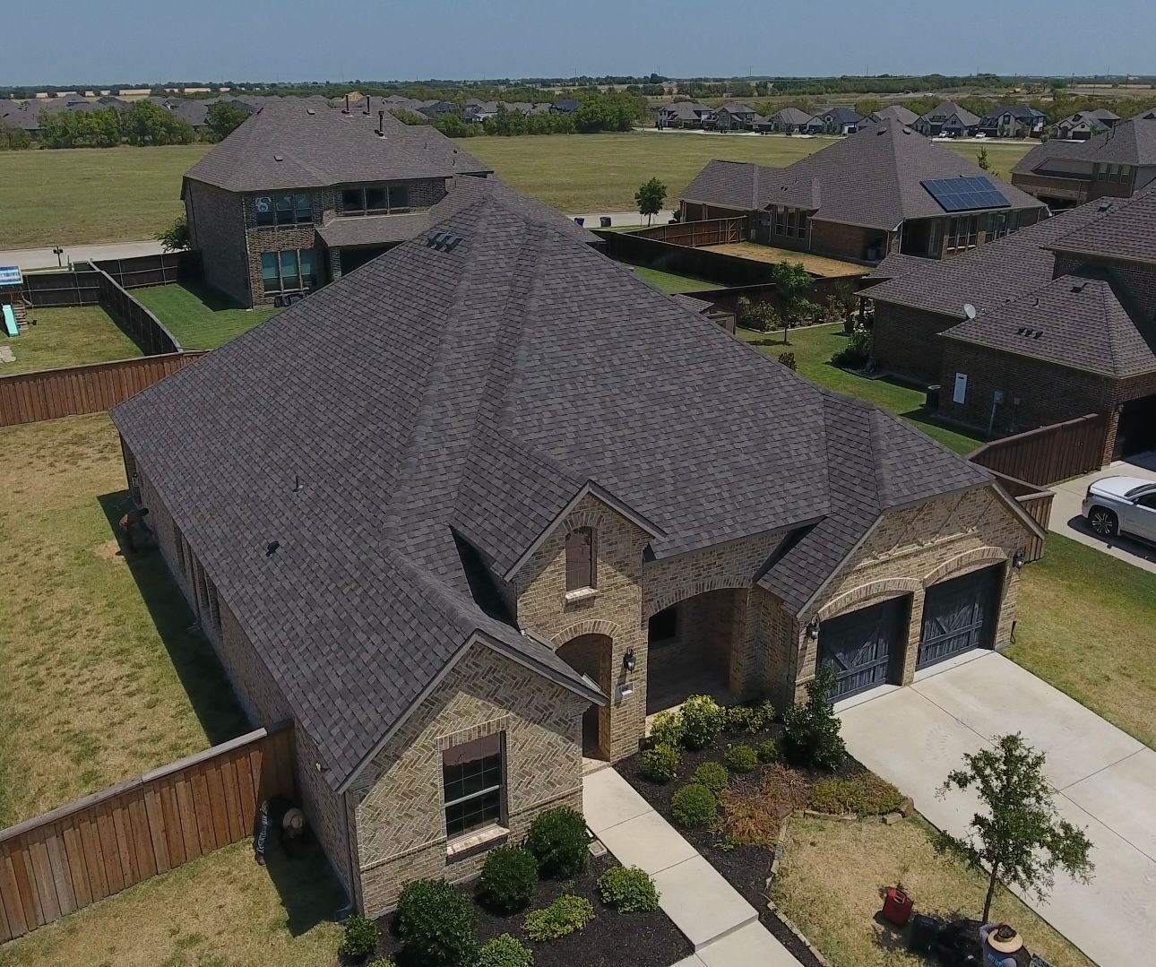Brick house with dark roof and attached garage, in suburban setting.