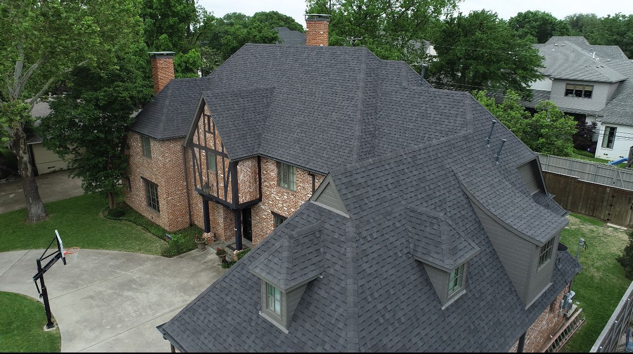 Two-story brick home with black roof, dormers, and chimney. Tudor style with a basketball hoop in the driveway.