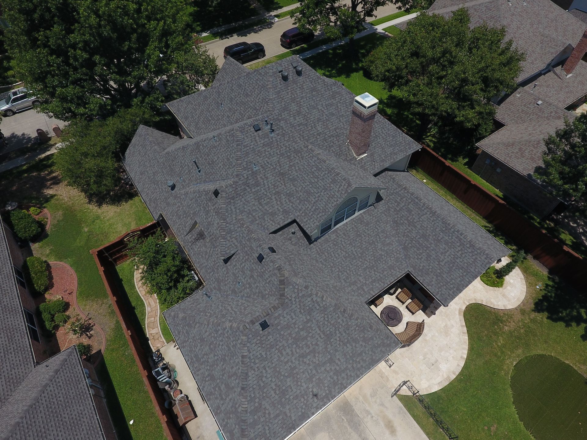 Aerial view of a gray-roofed house with a chimney, trees, and a backyard patio.