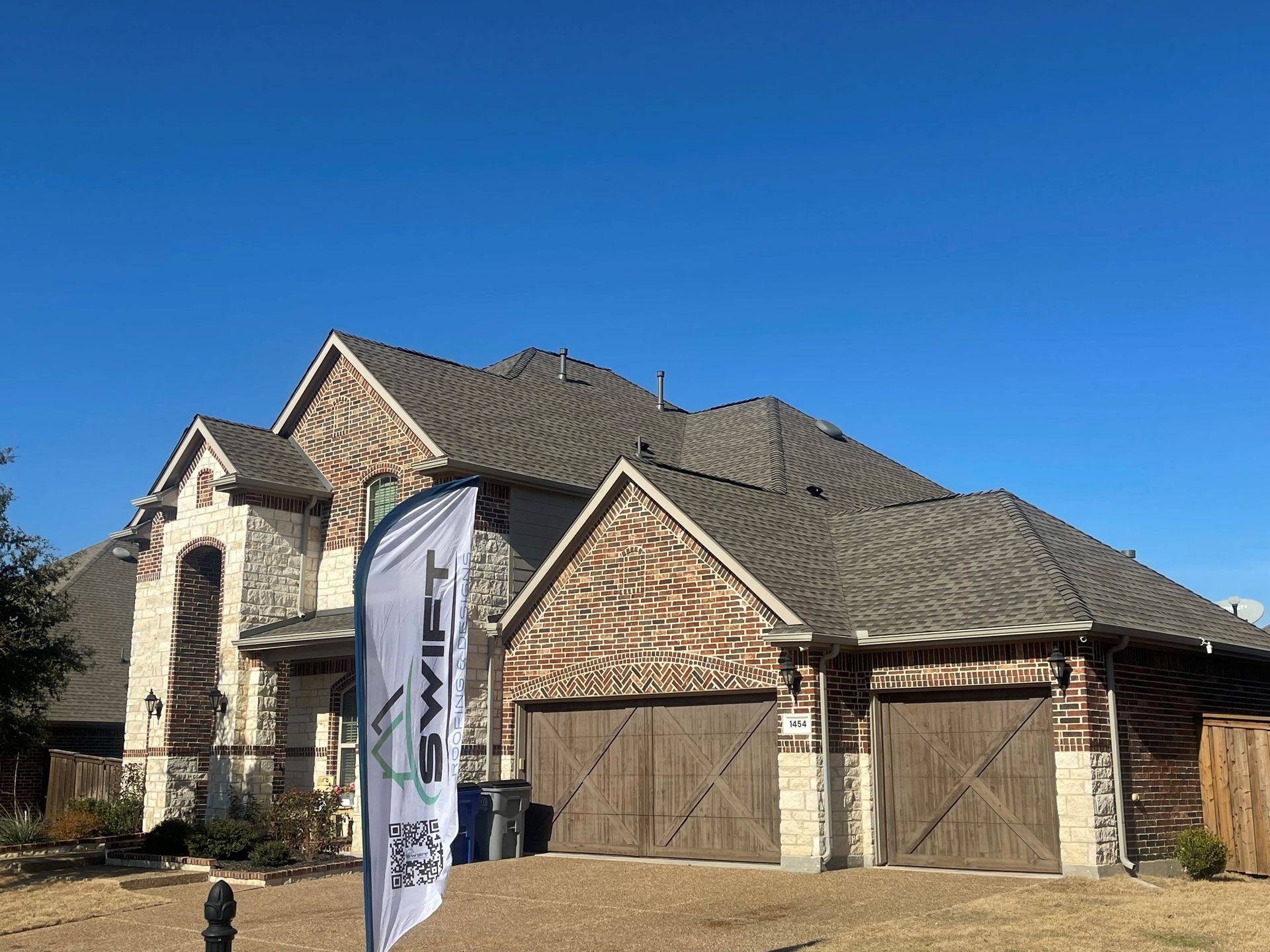 Two-story stone house with brown garage doors and a white banner in the front yard