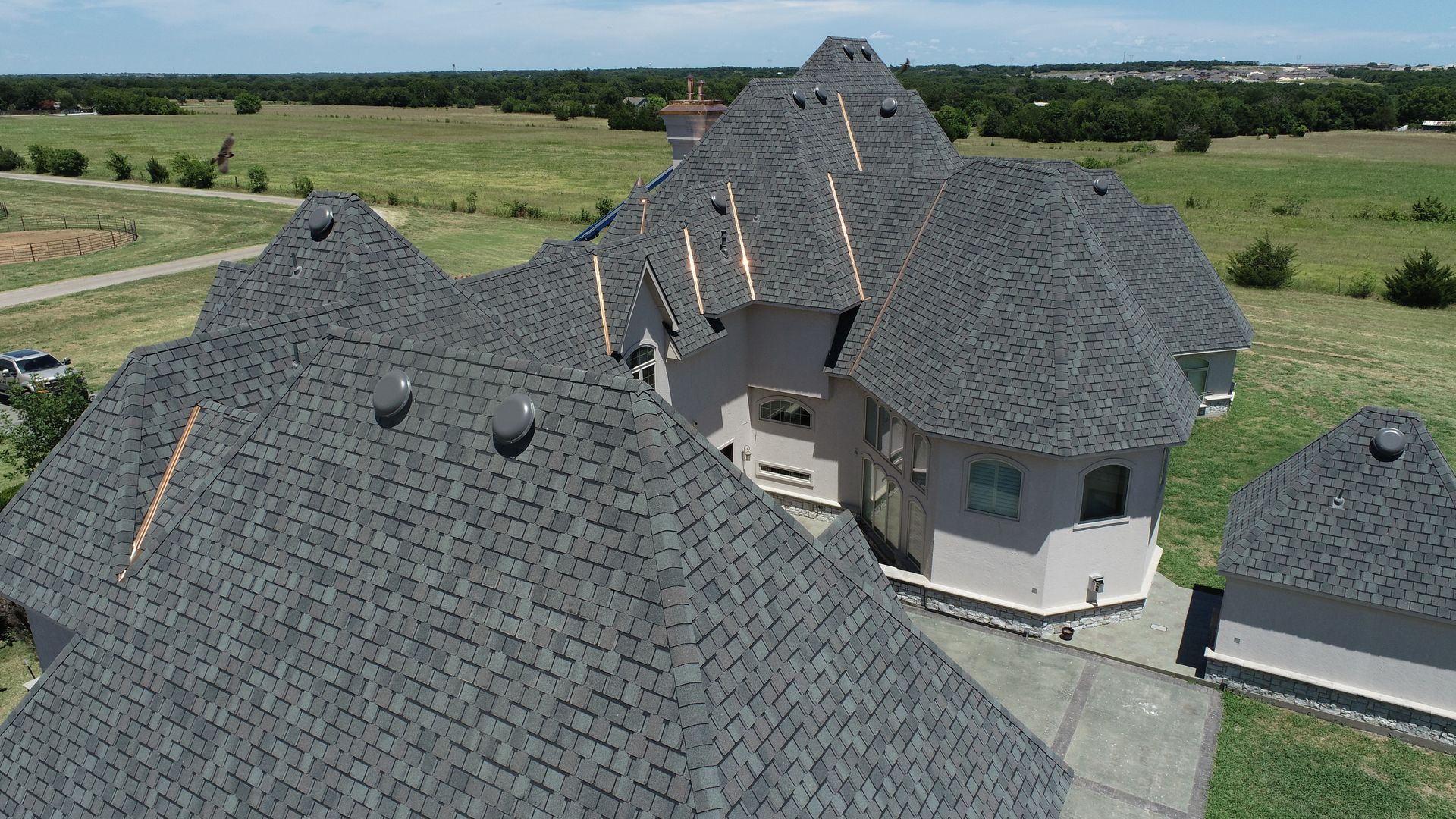 Aerial view of a large house with a complex, dark gray shingle roof.