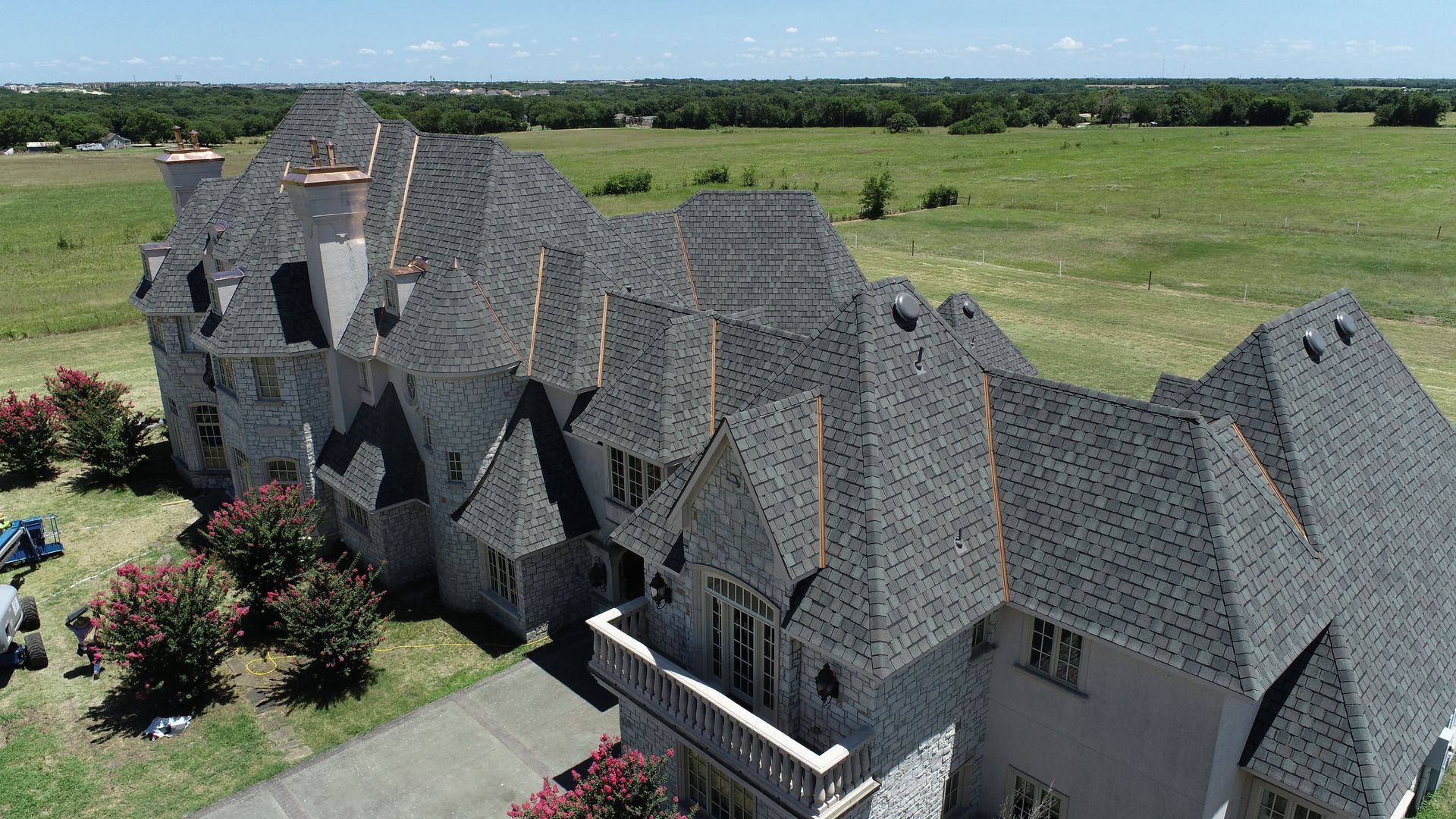 Aerial view of a large gray-roofed mansion surrounded by green lawns and landscaped gardens.