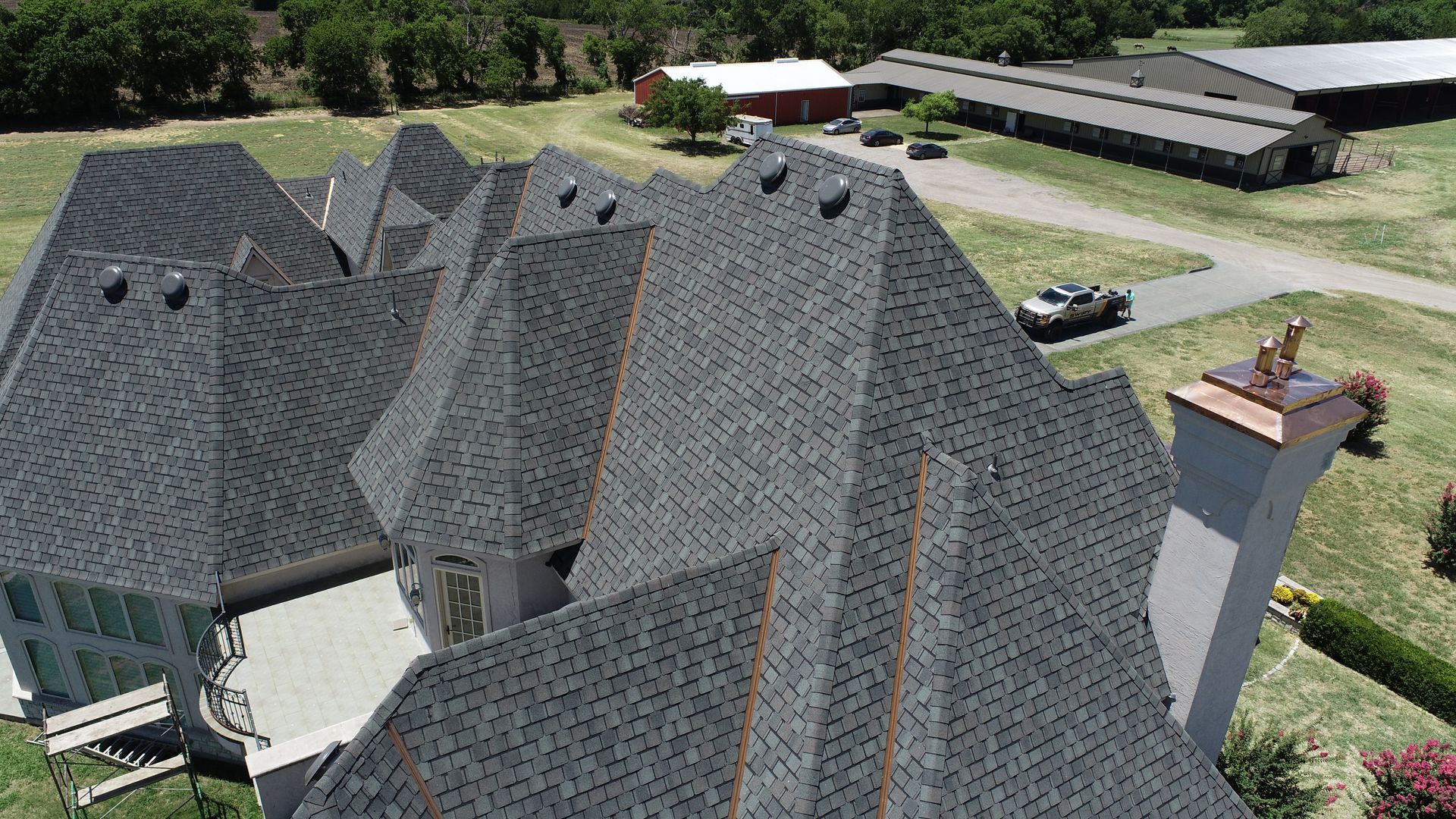 Aerial view of a complex roofline on a large house, with a chimney. Gray asphalt shingles.
