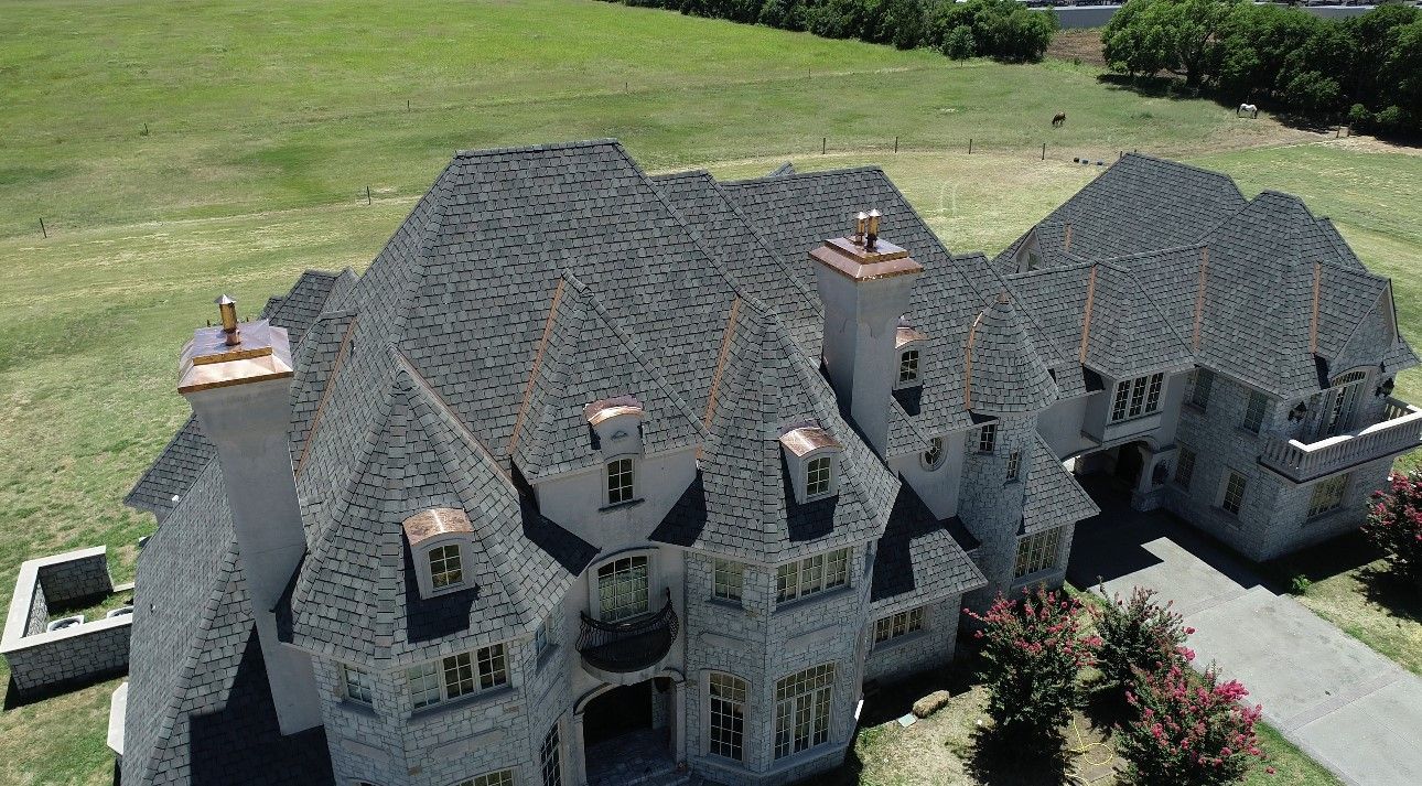 Large stone house with a dark gray roof and green yard.