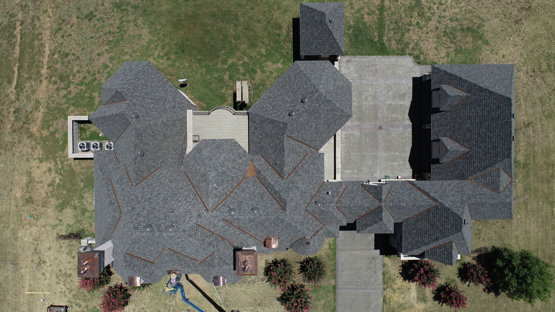 Aerial view of a large, gray-roofed house with a long driveway on a grassy lot.