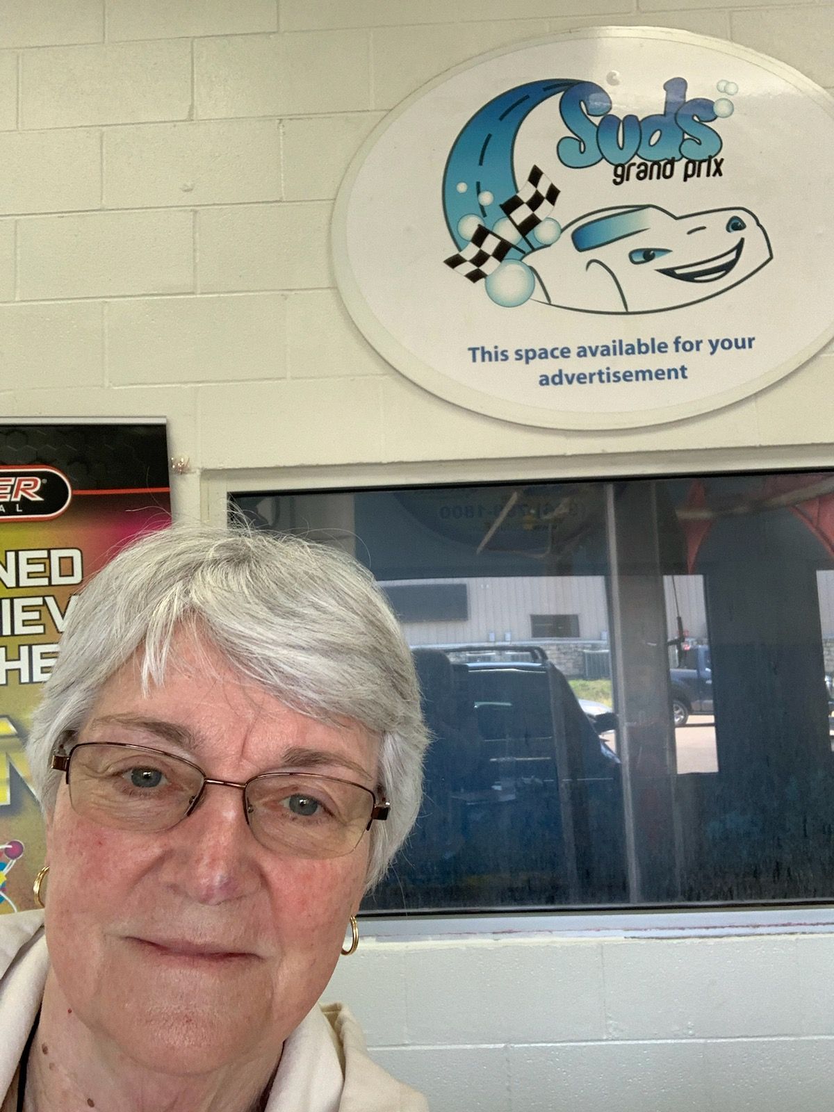 Woman wearing glasses in a car wash, with a business sign above her head.