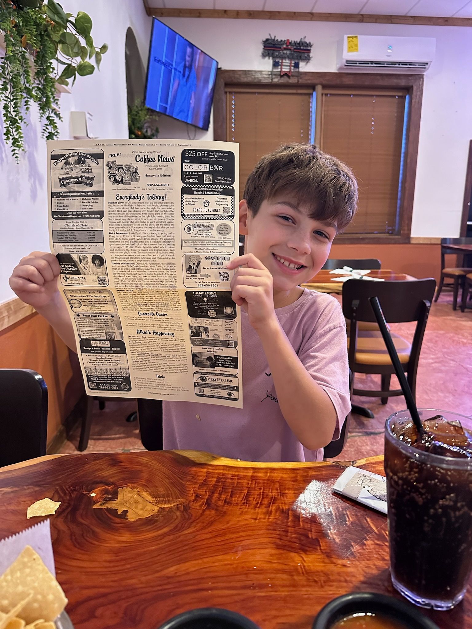Boy smiling, holding a restaurant menu. Sitting at a table with chips, salsa, and a drink.