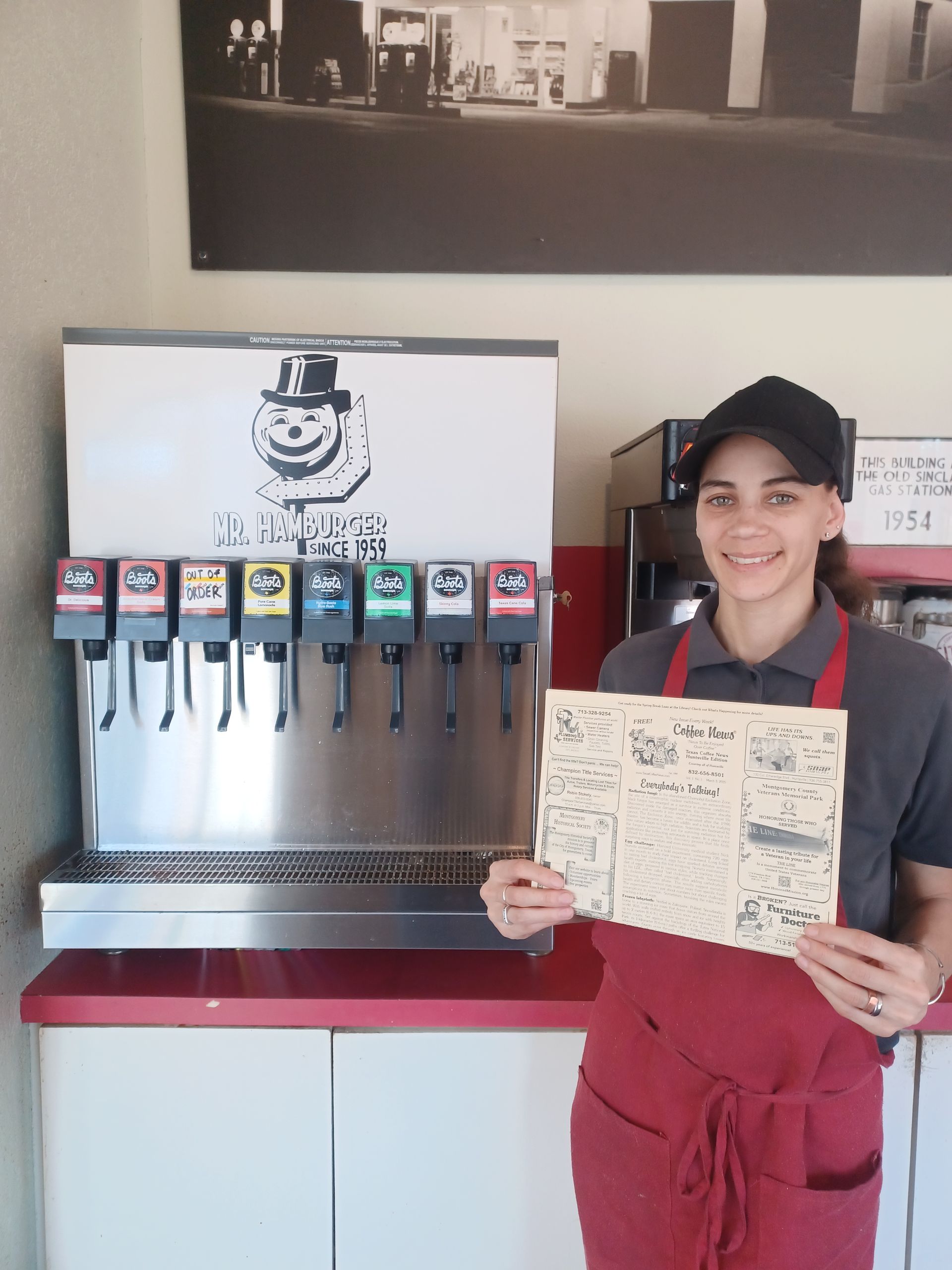 Woman in apron holds menu near soda fountain.