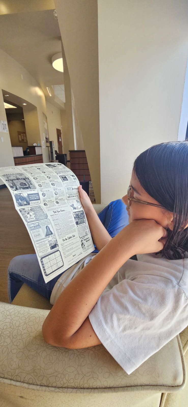 Person reading a newspaper while sitting on a couch indoors.