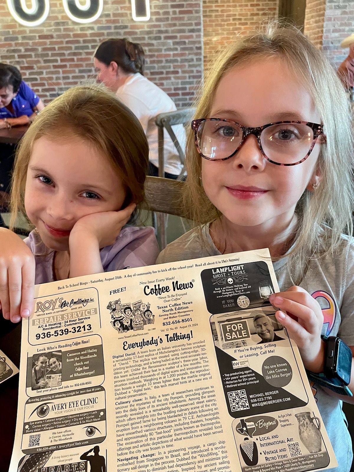 Two young girls holding a menu, smiling at a restaurant table.