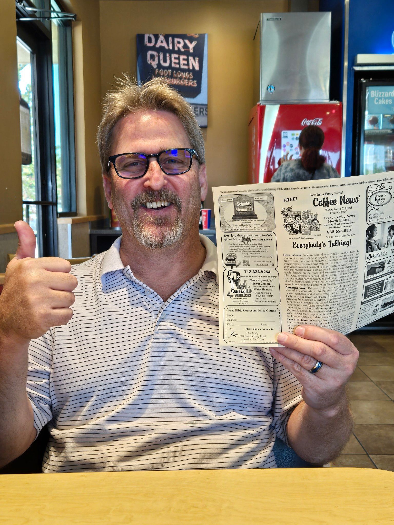 Man holding a newspaper, giving a thumbs up in a Dairy Queen.