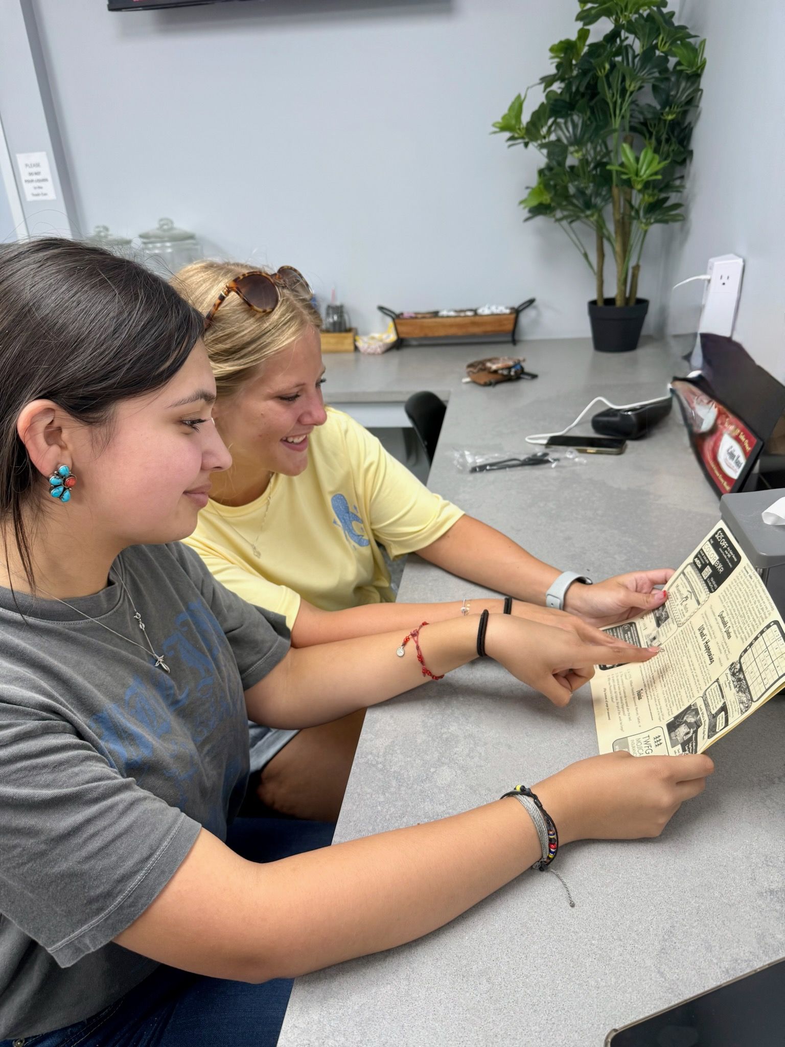 Two people looking at a printed paper, pointing. Gray counter, bright room.