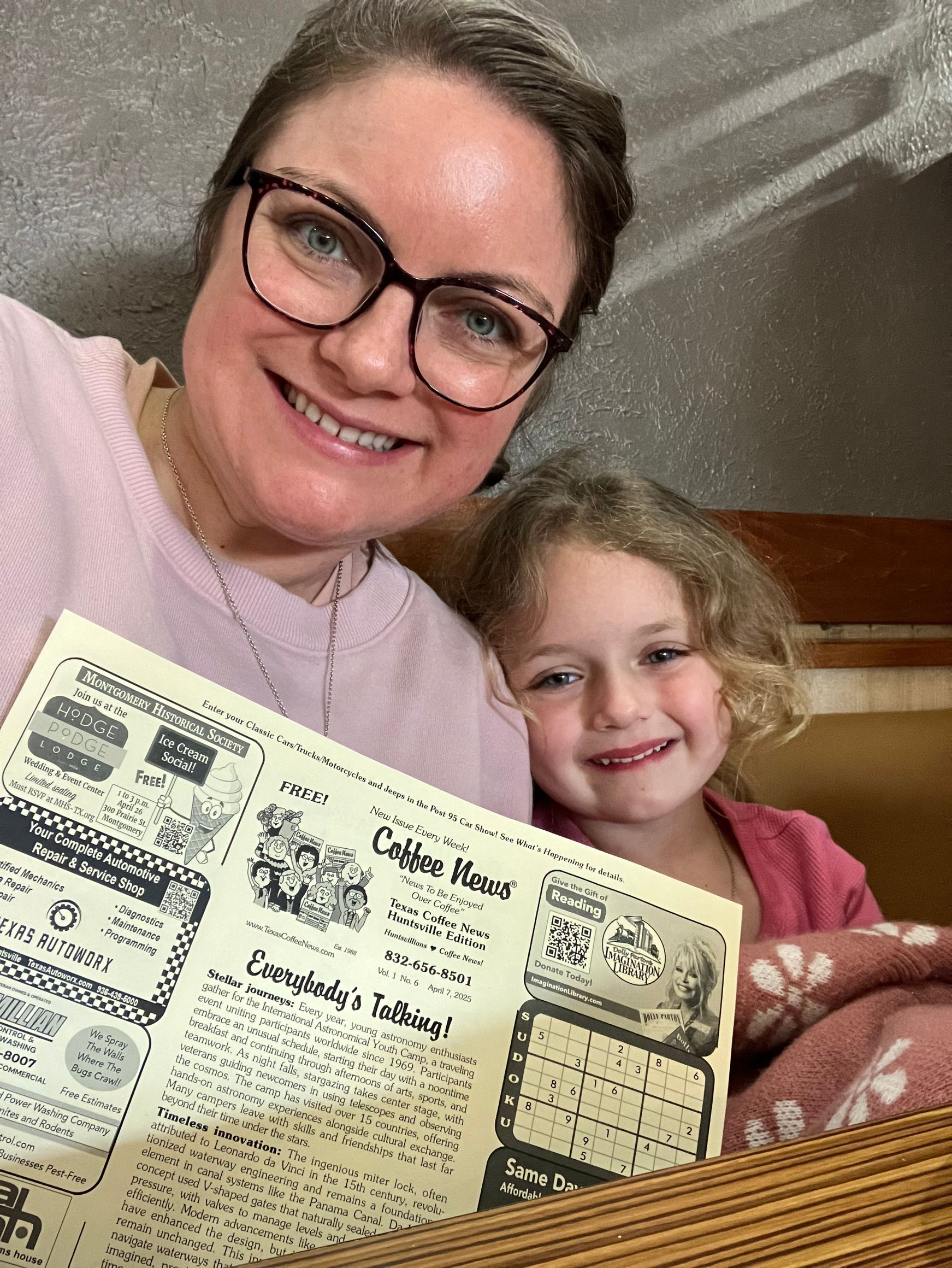 Woman and young child smiling, holding a vintage newspaper, indoors.