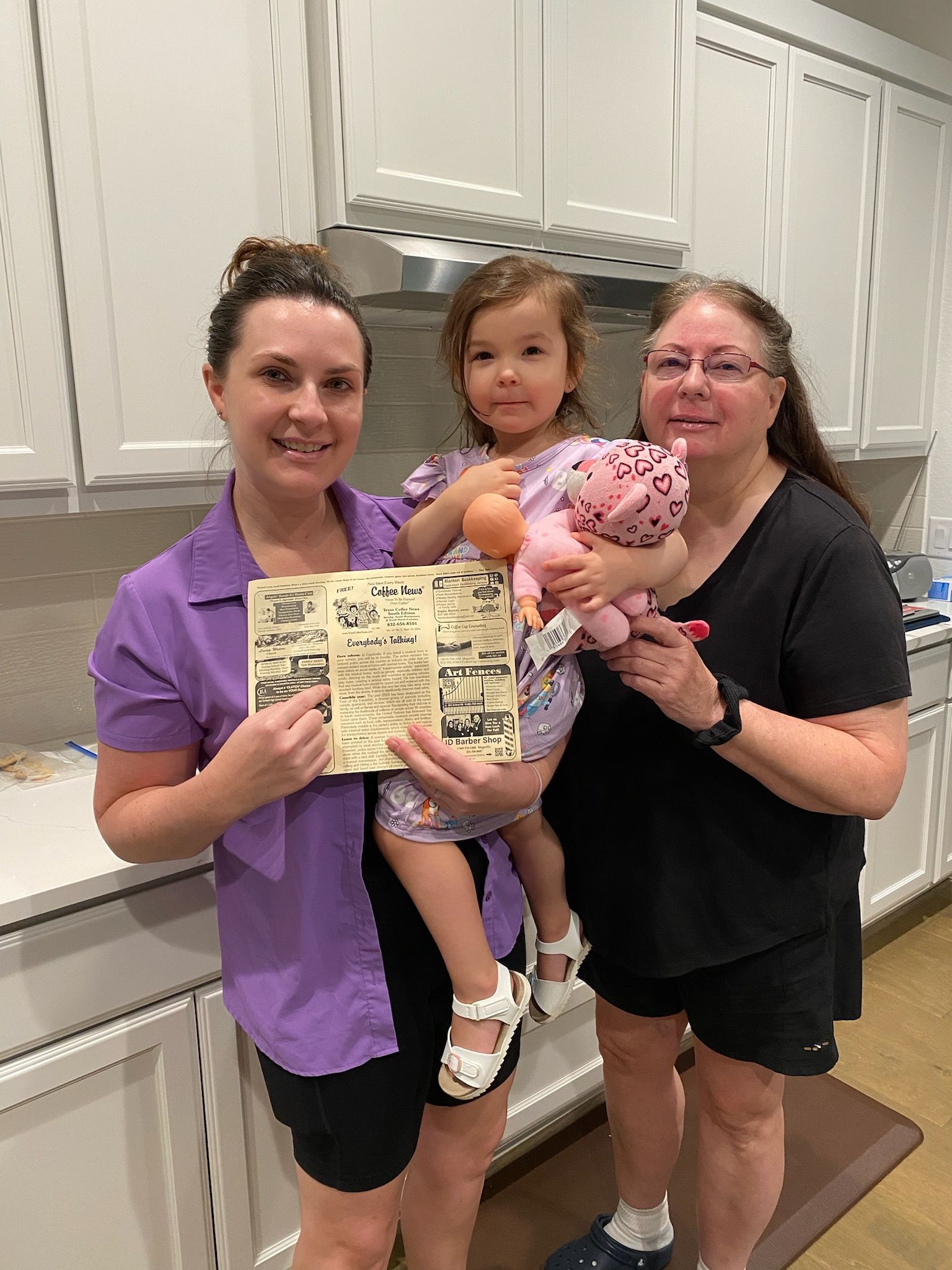 Three people in a kitchen holding a paper. 