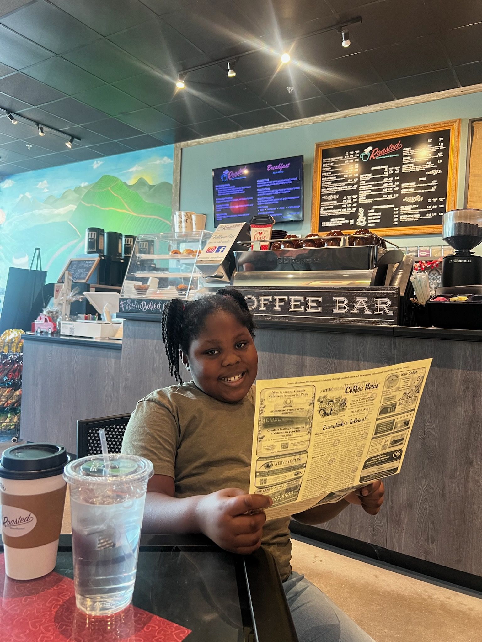 Young person smiling, reading menu in a coffee shop. Coffee bar, drink visible.