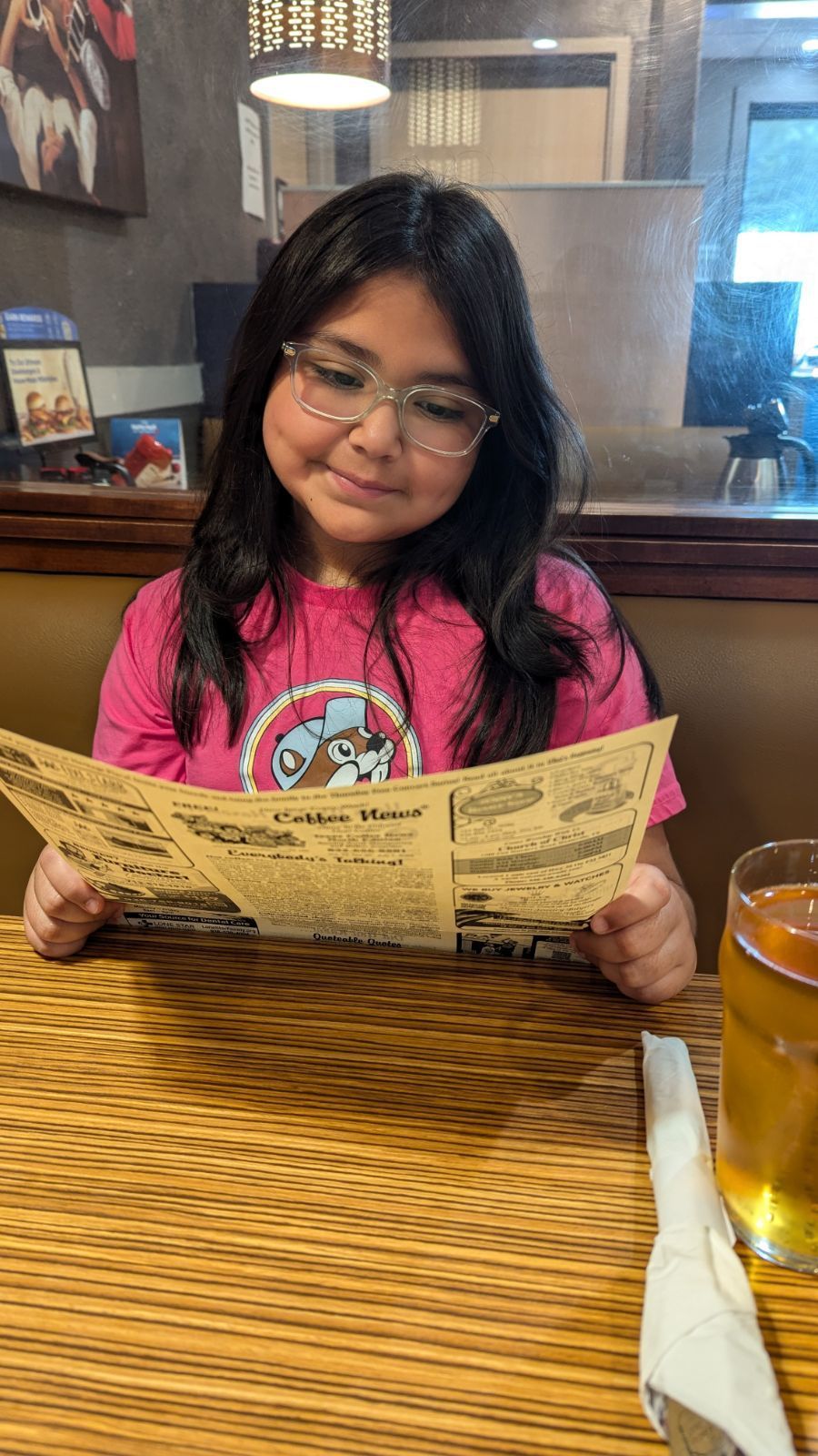 Young person with glasses reviews a restaurant menu, seated at a table.