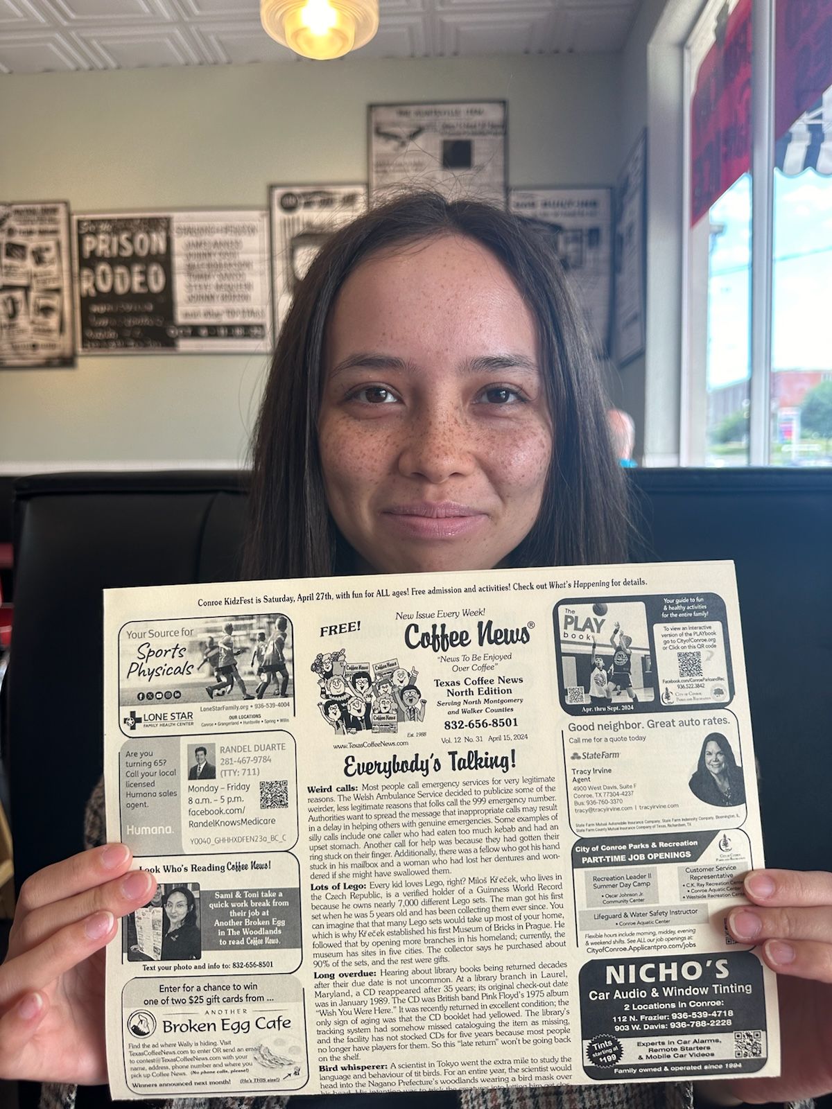 Woman holding a printed black-and-white restaurant placemat featuring articles, ads, and a central illustration.