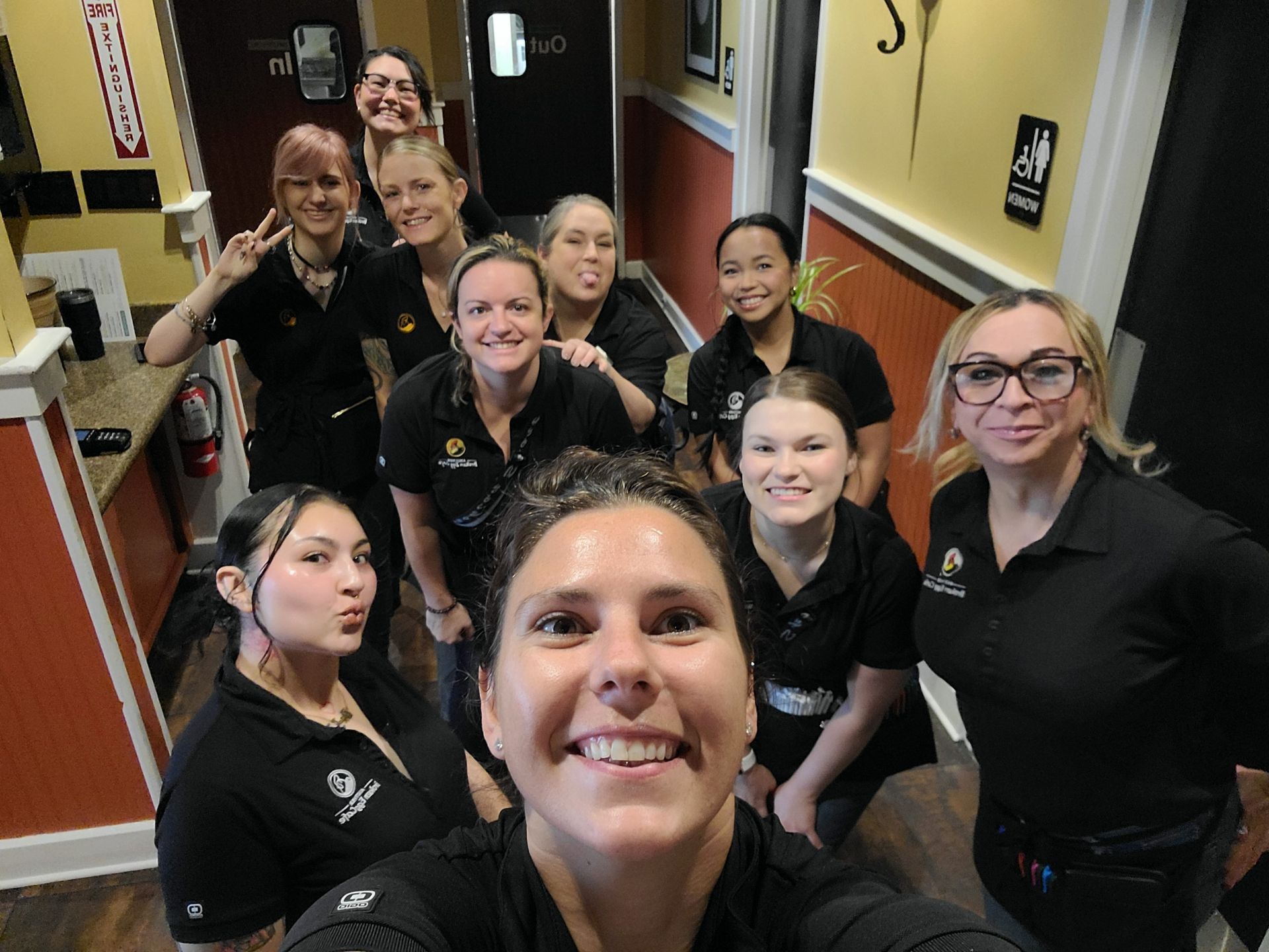 Group of people in black shirts smiling and posing for a selfie in a hallway.