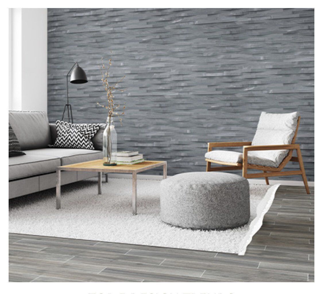 Living room with gray stone wall, gray sofa, wooden chair, pouf, and rug.