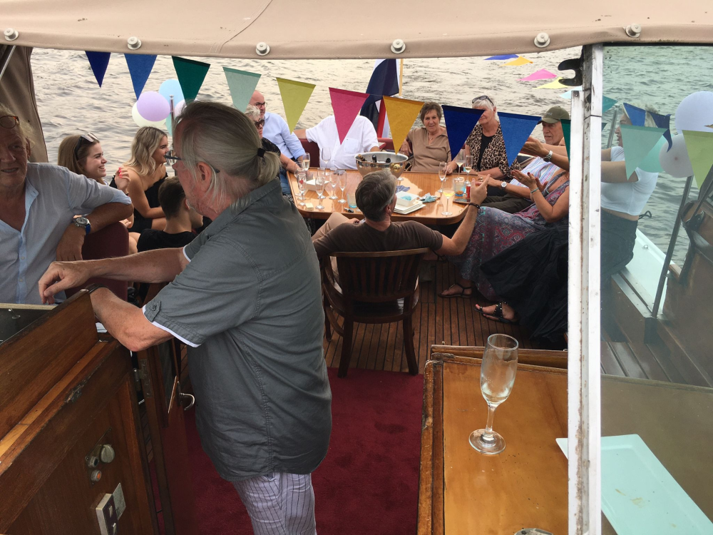 Een groep mensen verzamelt zich op het dek van een boot die versierd is met kleurrijke vlaggetjes voor een gezellig samenzijn.