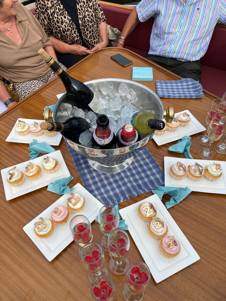 Een centrale ijsemmer met wijnflessen, omringd door schalen met cupcakes en glazen frambozen op een houten tafel.